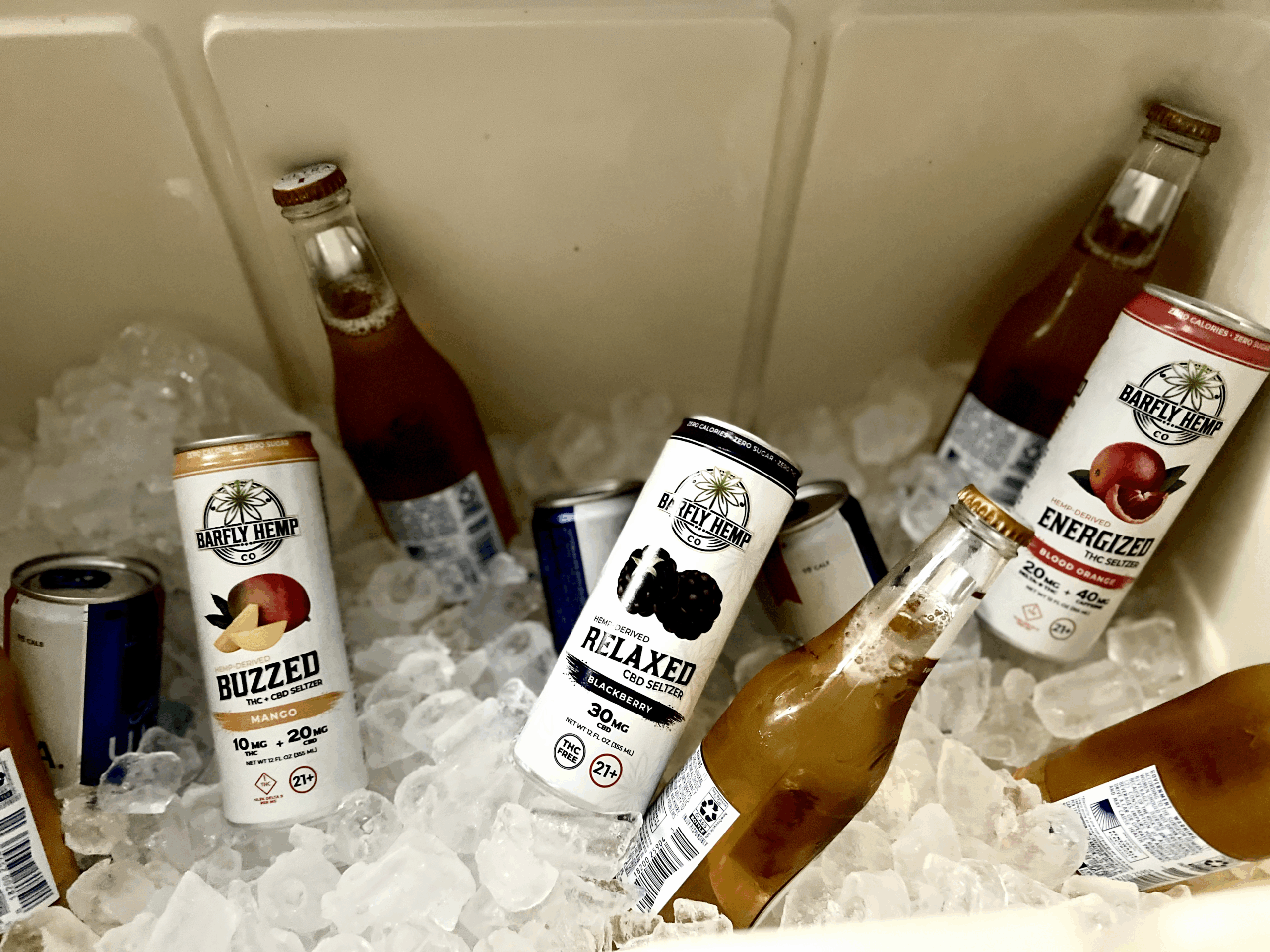 Cans of Barfly Hemp Co. Buzzed Mango, Relaxed Blackberry, and Energized Blood Orange seltzers chilling in ice alongside bottled drinks inside a cooler.